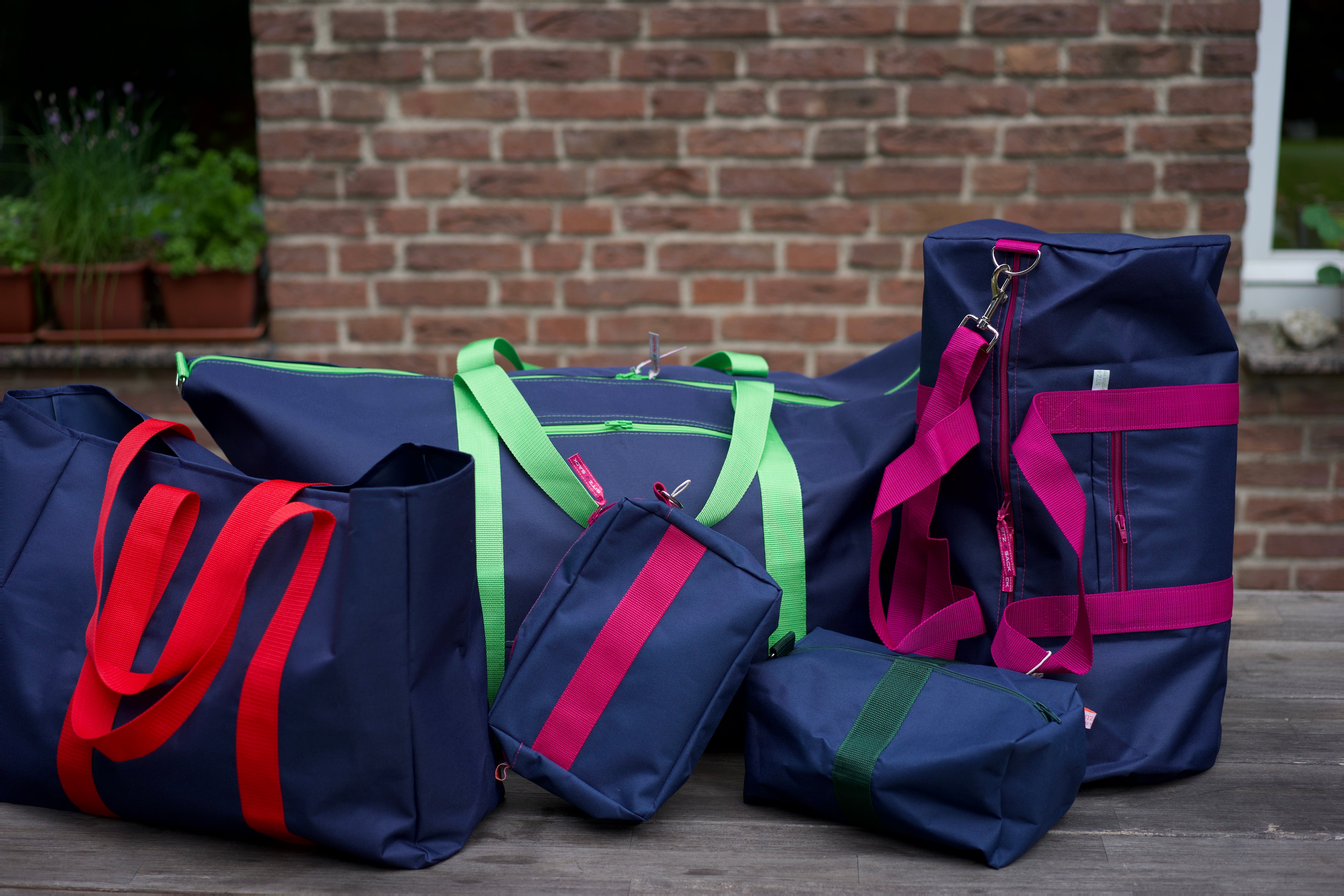 Fünf Taschen von Sitz & Sack in dunkelblau mit farbigen Gurtbändern: Shopper, Weekender, Kulturbeutel, Sporttasche und Reisetasche