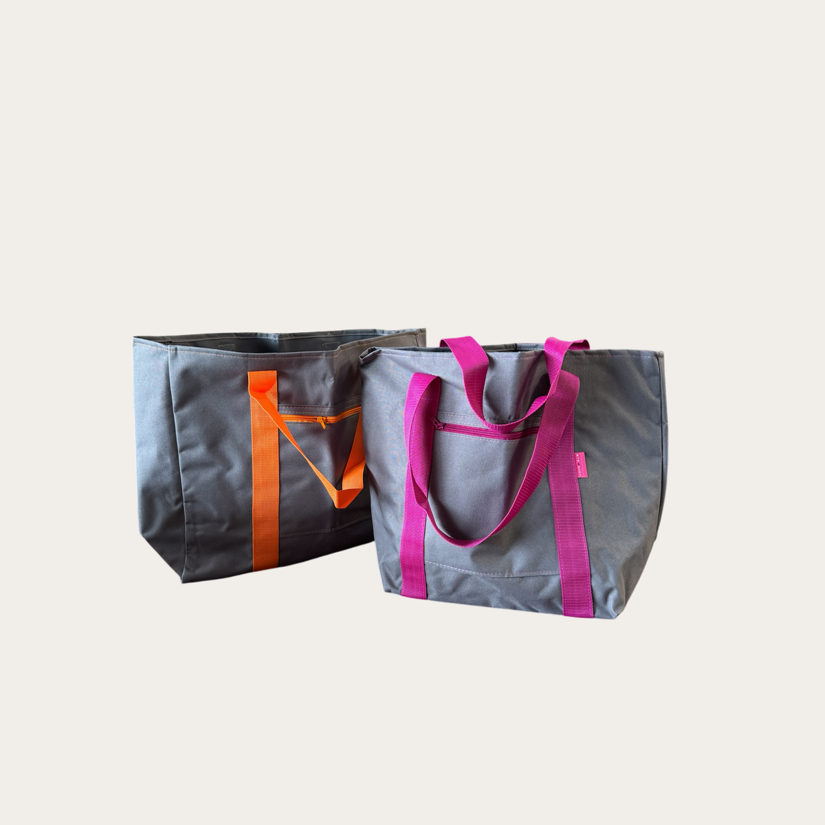 Zwei Shopper in grau, einer mit orangem, einer mit magentafarbenem Gurtband
