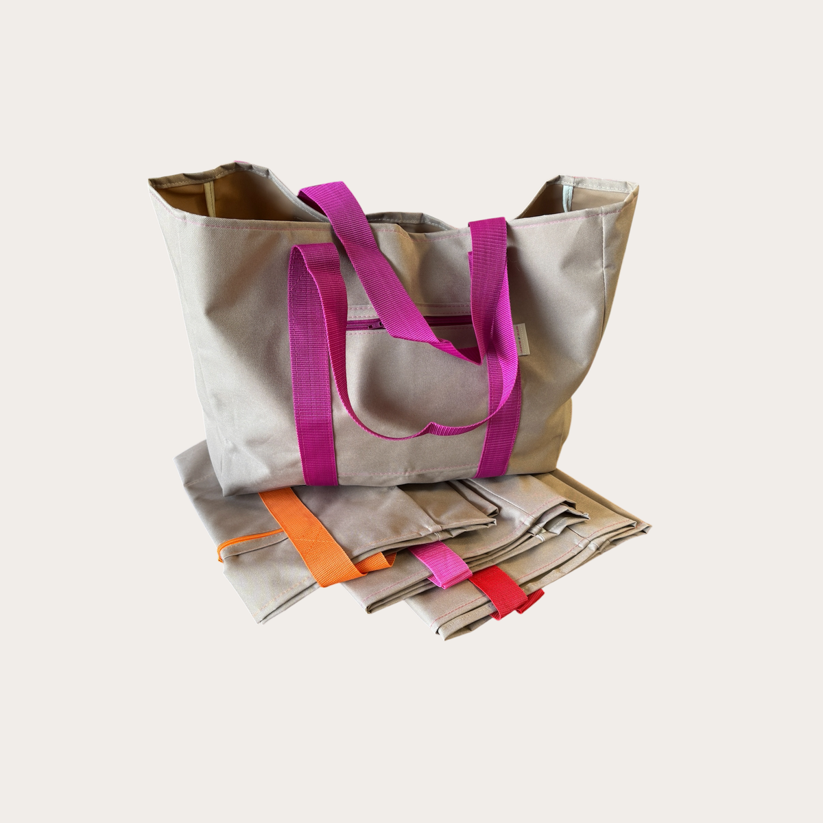 Shopper in beige mit magentafarbenem Gurtband, davor zwei zusammengefaltete Shopper